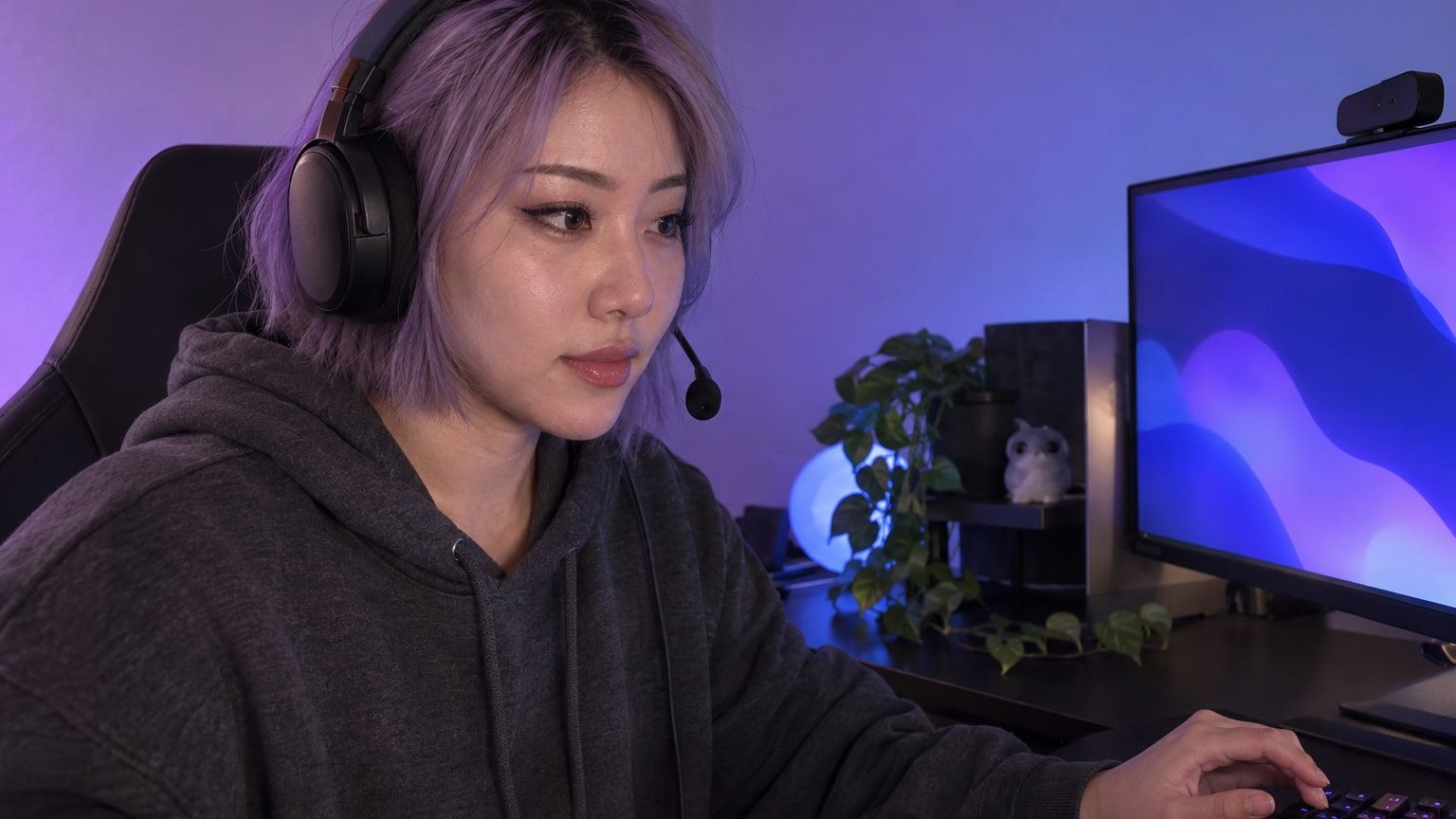 Woman with a lavender bob and gaming headset plays at a desk in purple light.